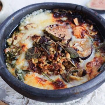 Baked cheese dish with figs, herbs, and nuts in a black bowl.