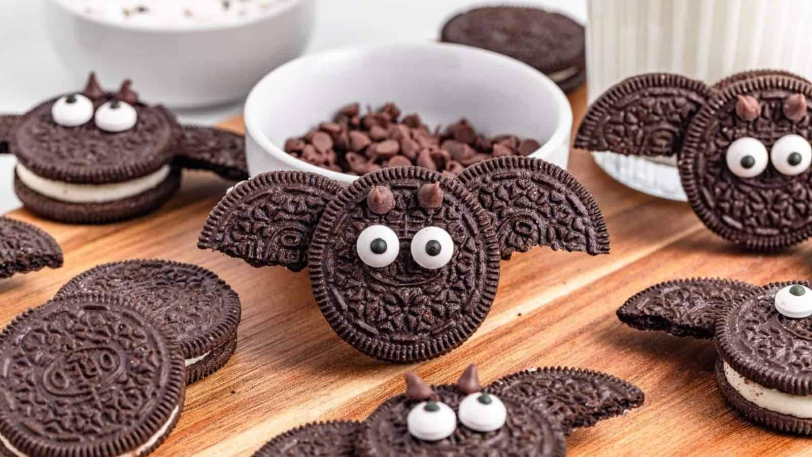 Bat-shaped Oreo cookies with candy eyes and chocolate chip ears on a wooden board.