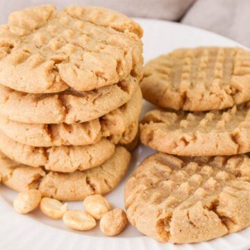 A plate of peanut butter cookies with a few peanuts scattered beside them.