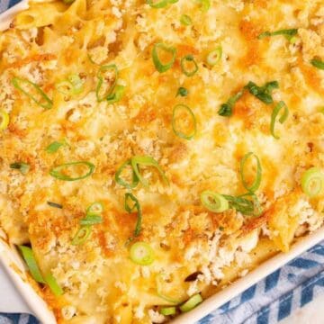Baked casserole topped with melted cheese, breadcrumbs, and chopped green onions in a white dish on a blue cloth.