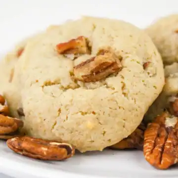Two pecan cookies on a white plate, surrounded by whole pecan nuts.