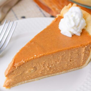 A slice of peanut butter pie with whipped cream on top, served on a white plate with a fork beside it.