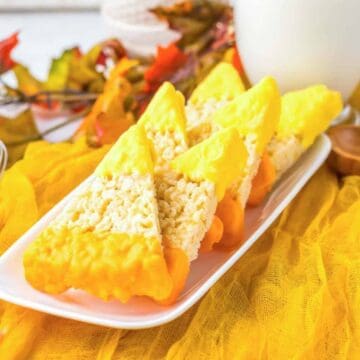 Rice Krispies treats dipped in yellow and orange chocolate, arranged on a white plate with fall decor.