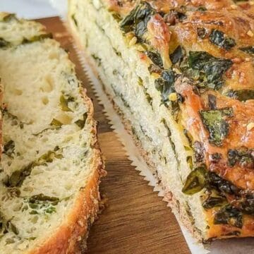 Sliced herb bread with a golden crust and green herbs visible throughout, on a wooden cutting board.