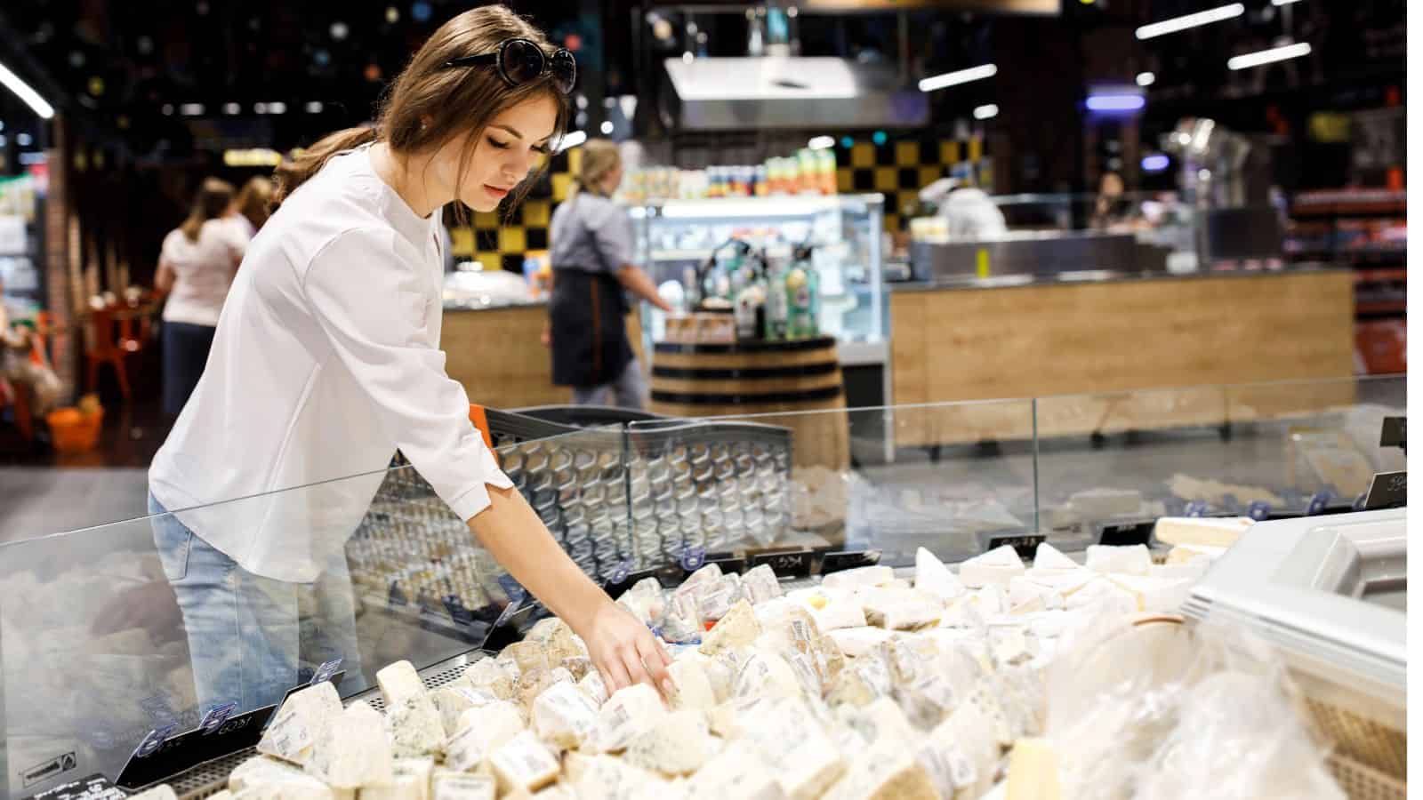A woman selects packaged cheese from a display case in a grocery store, staying mindful of the recent cheese recall in Canada.
