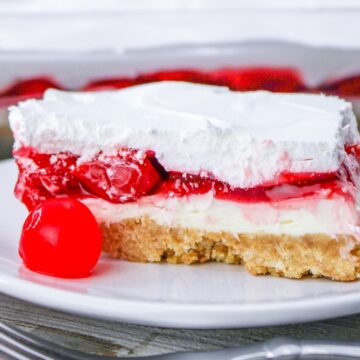 A slice of cherry dessert with whipped topping and a cherry on a white plate.