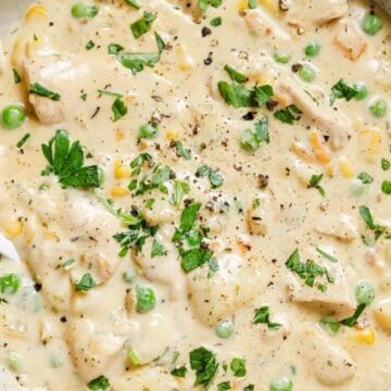Creamy chicken and vegetable soup garnished with chopped parsley and black pepper in a bowl with a spoon.