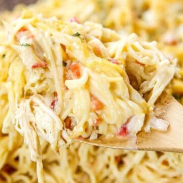 A wooden spoon lifts creamy baked spaghetti with cheese and bits of vegetables.