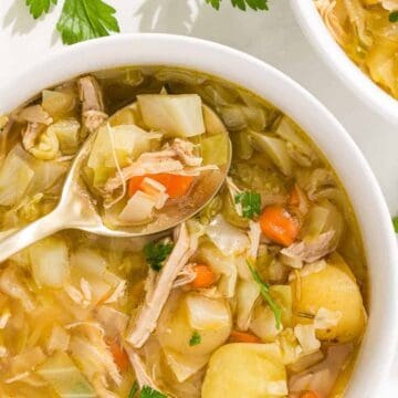 Bowl of vegetable and chicken soup with potatoes, carrots, and herbs, garnished with parsley.