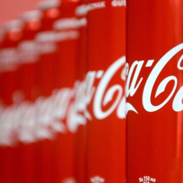 Rows of red Coca-Cola cans with white logo, shown in close-up and fading into the background—a reminder of recent Coca-Cola recalls over possible metal contamination.