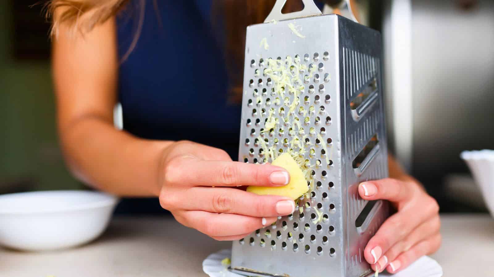 A person grating cheese on a metal grater over a white plate in a kitchen—perfect inspiration for gifts for cheese lovers.