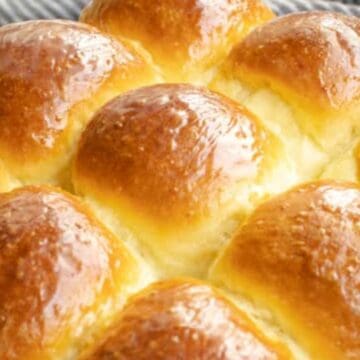 Golden, shiny, freshly baked dinner rolls closely packed together on a white plate.