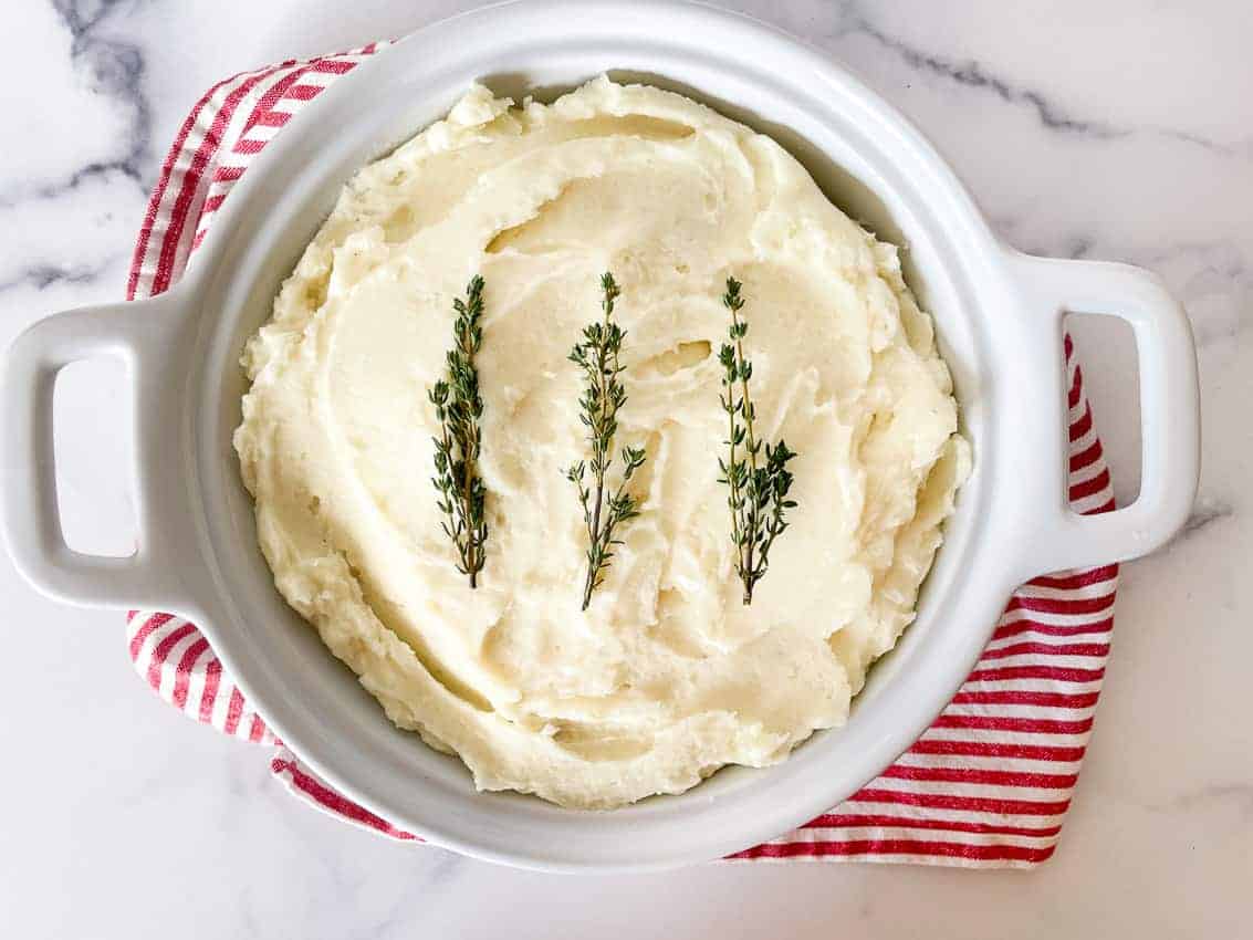 A bowl of whipped potatoes with butter and herbs on top. 