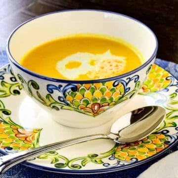 A bowl of creamy soup with a swirl of cream, served on a colorful saucer with a spoon.
