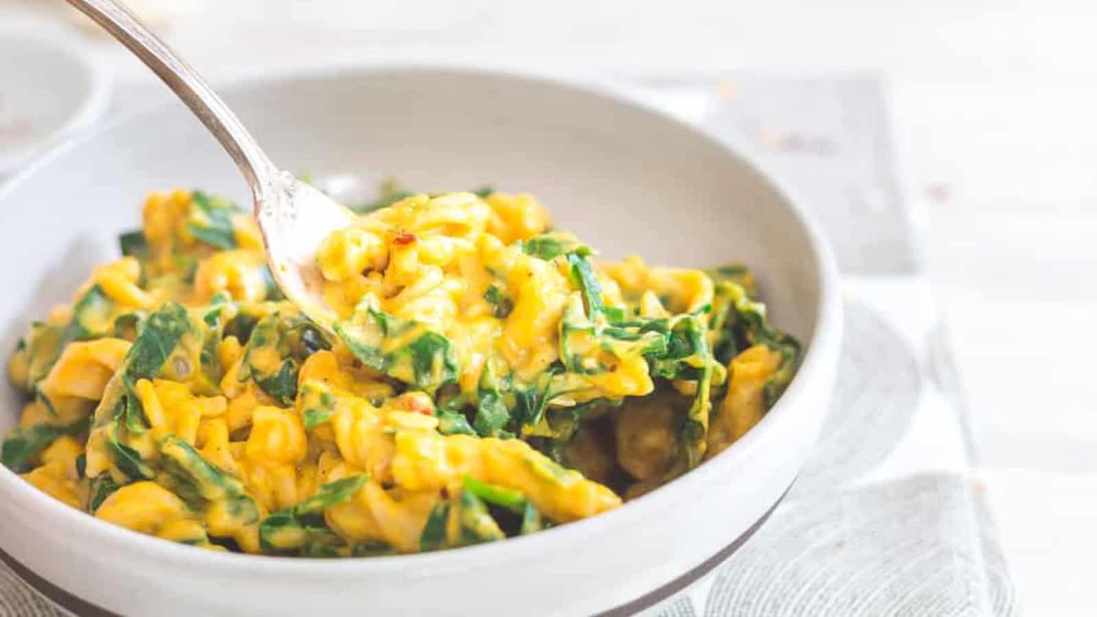 Creamy pumpkin pasta with garlic and tuscan kale in a bowl with a spoon.