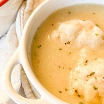 White bowl of creamy soup with two fluffy dumplings, sprinkled with herbs, on a white towel.