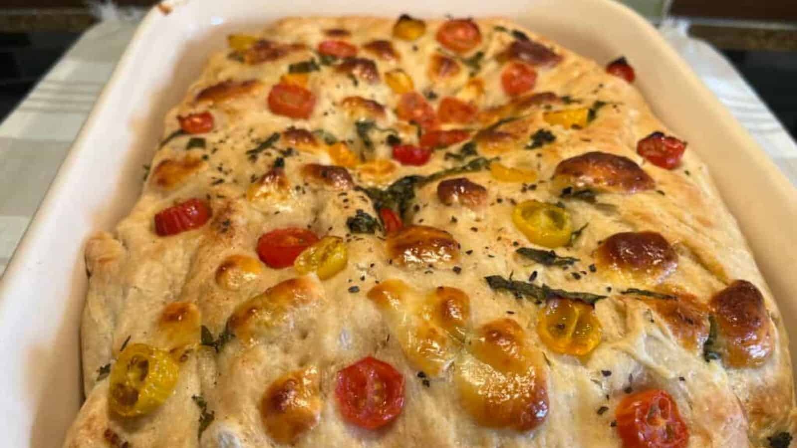 Freshly baked focaccia with cherry tomatoes and herbs in a rectangular baking dish.