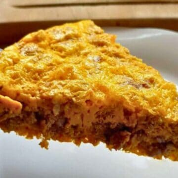 A slice of cheesy, baked casserole with ground meat being served on a spatula over a white plate.