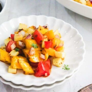 A white plate with a colorful fruit and vegetable salad, including mango, apple, and red bell pepper.