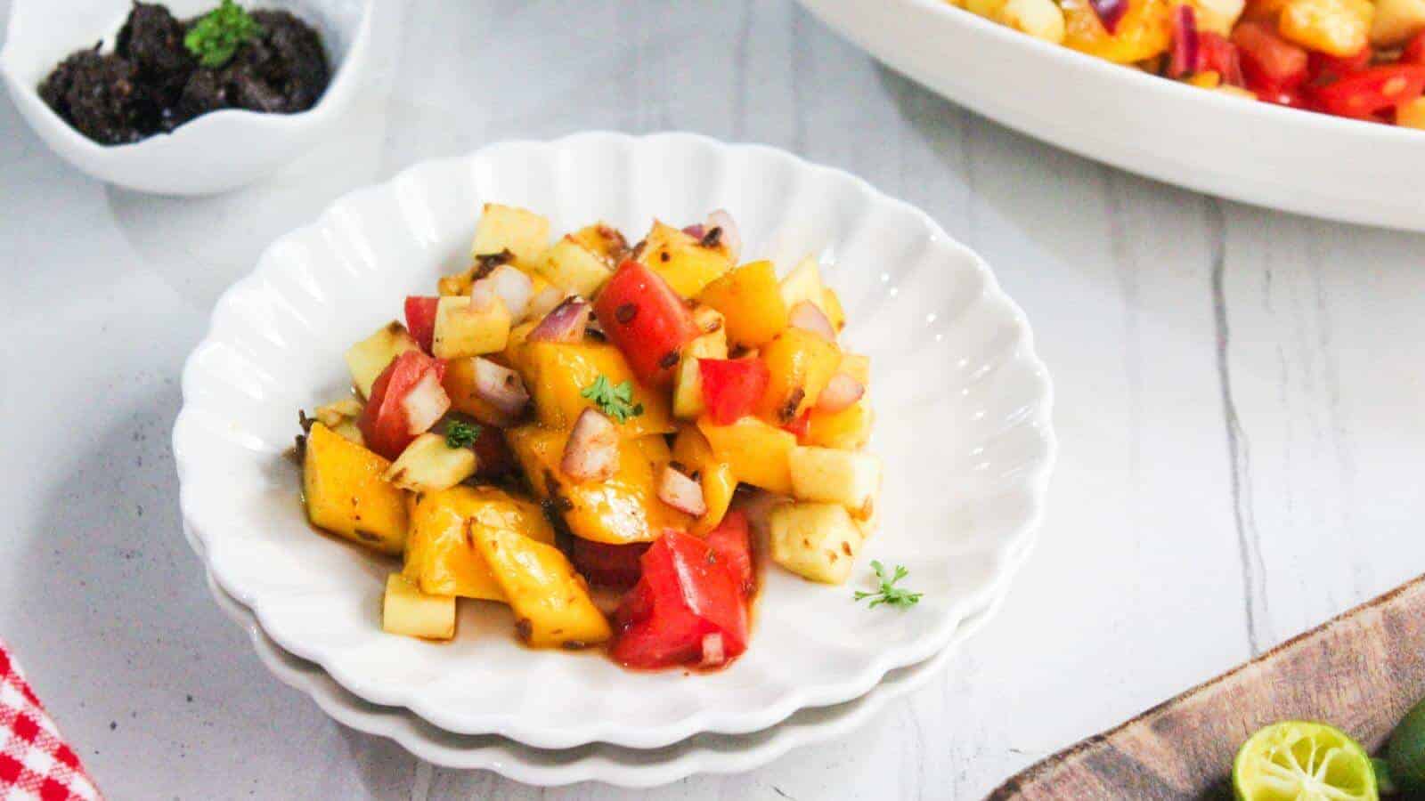 A white plate with a mixed fruit and vegetable salad, including mango, apple, red bell pepper, and onions, garnished with herbs.