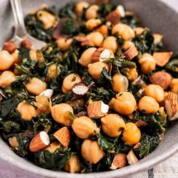A bowl of chickpea and spinach salad with chopped almonds, served with a fork.