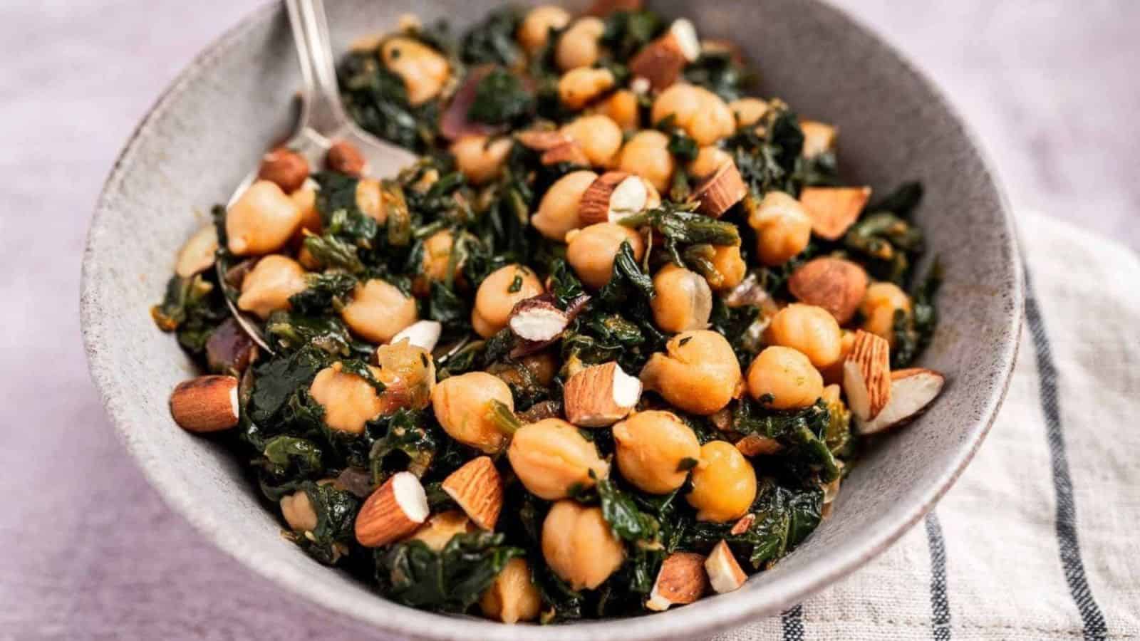 A bowl of chickpea and spinach salad with chopped almonds, served with a fork.