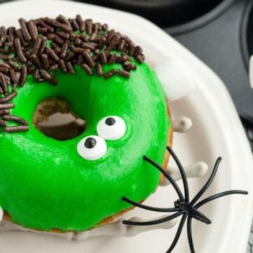 A donut decorated with green icing, candy eyes, chocolate sprinkles, and marshmallows to look like a monster.