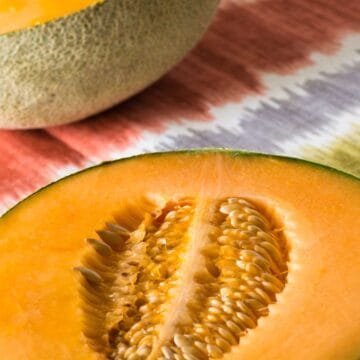 Close-up of two cantaloupe halves on a colorful, patterned cloth surface.