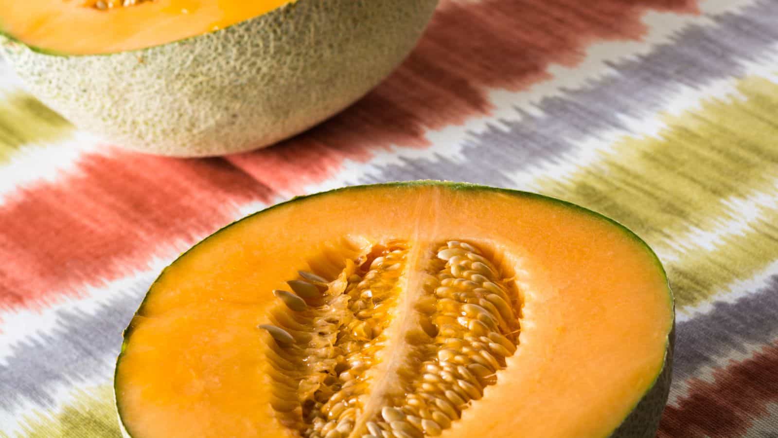 Close-up of two cantaloupe halves on a colorful, patterned cloth surface.
