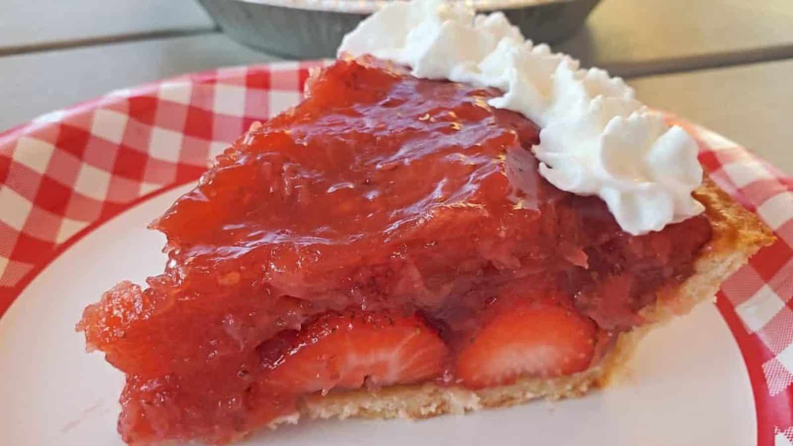 Slice of strawberry pie on a plate with the whole pie in the background.