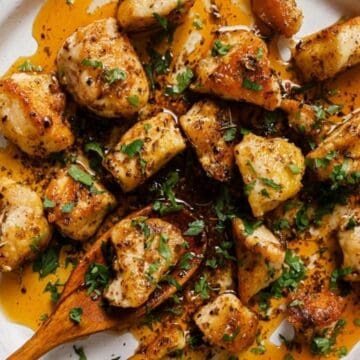Plate of seasoned, grilled chicken pieces garnished with herbs, with a wooden spoon on the side.