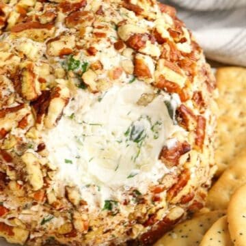 A cheese ball coated in chopped nuts, served with round and rectangular crackers on a white plate.