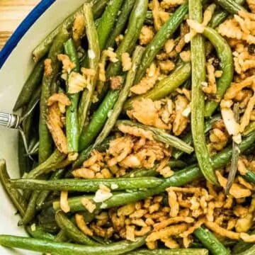 Green bean casserole topped with crispy fried onions in a blue-rimmed baking dish with a serving spoon.