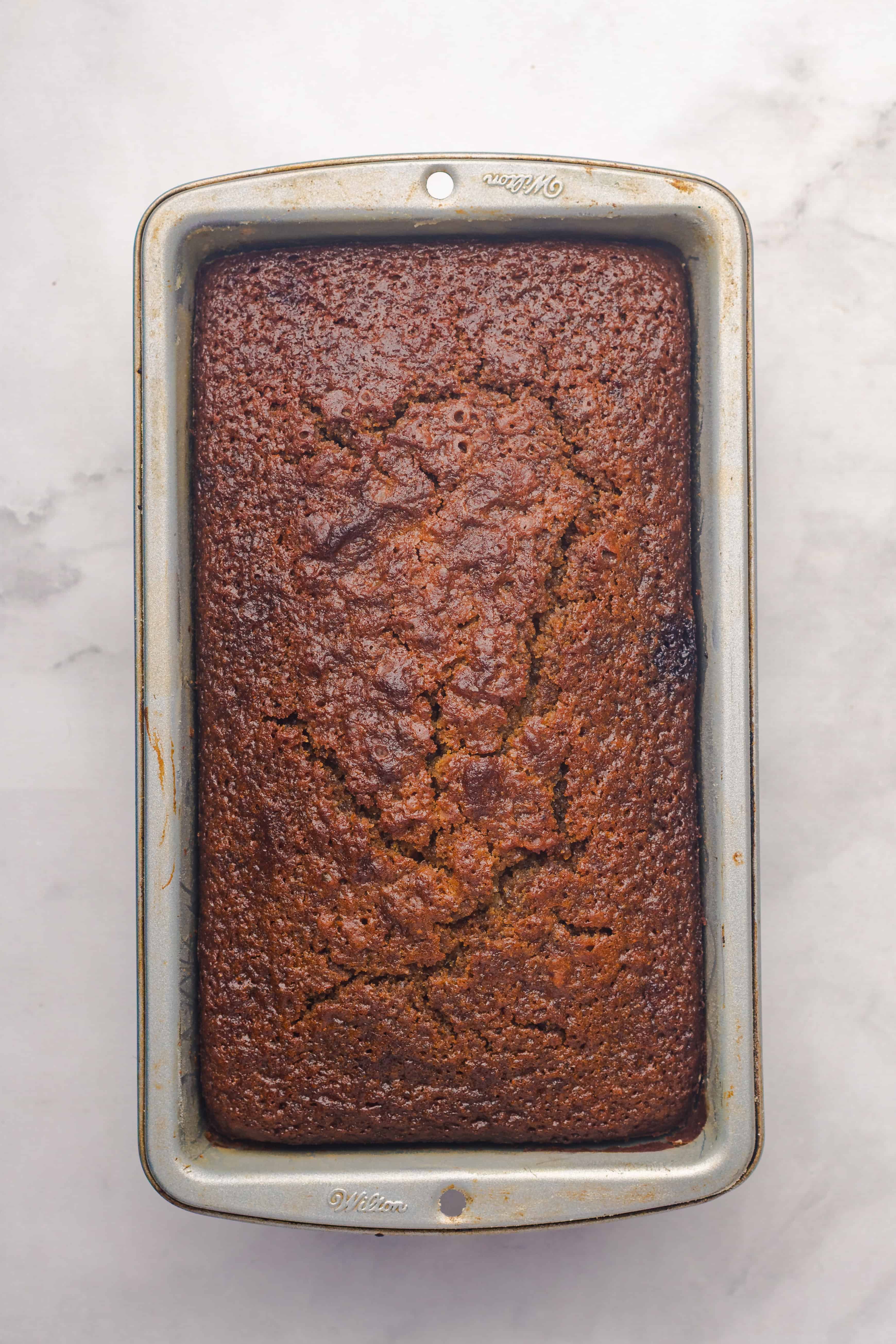 A loaf of banana bread in a metal pan on a light marble surface, reminiscent of a classic Gingerbread Loaf.