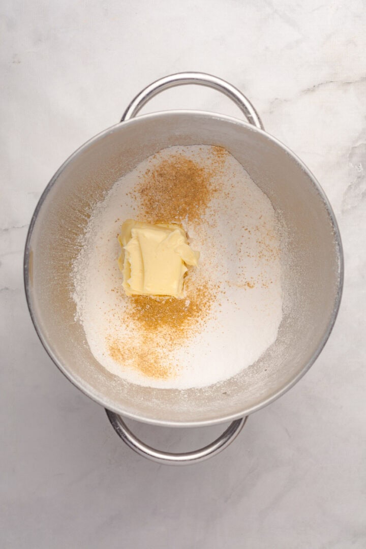 A metal mixing bowl with flour, a chunk of butter, and a sprinkle of brown sugar on a light surface—perfect for starting a delicious Gingerbread Loaf.