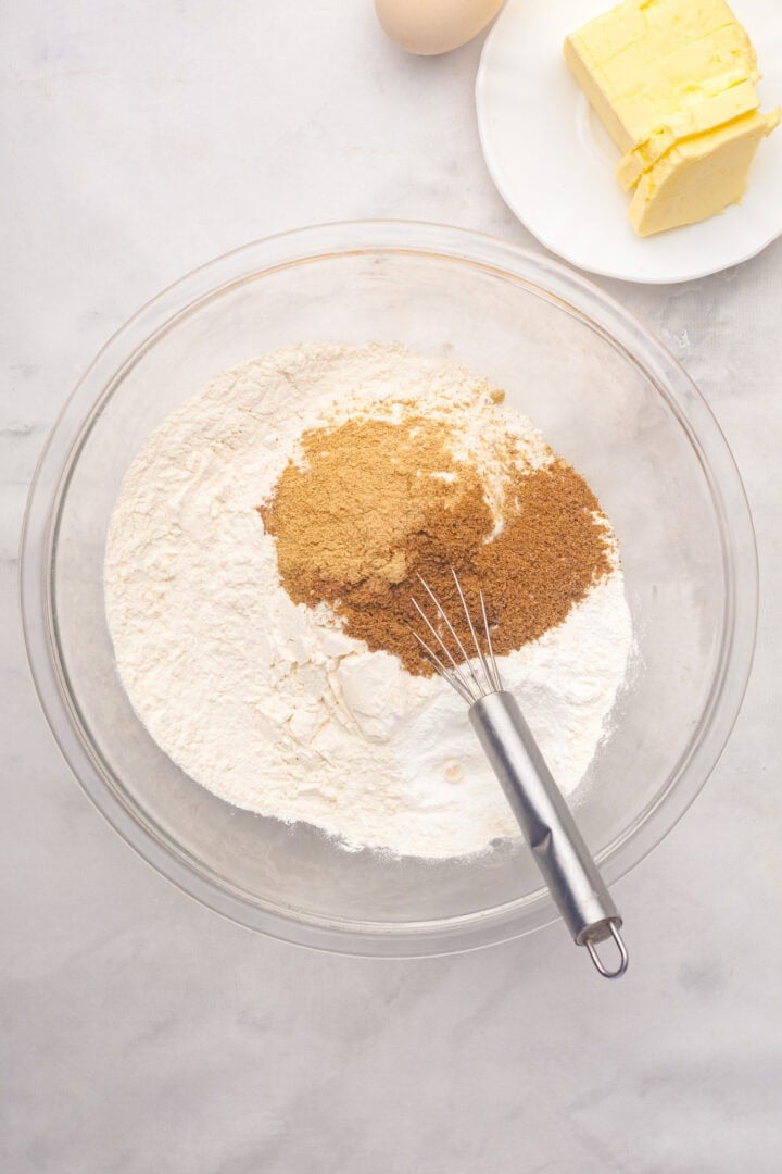 A mixing bowl with flour and brown sugar, a whisk, butter, and an egg on a light surface—perfect for starting your Gingerbread Loaf recipe.