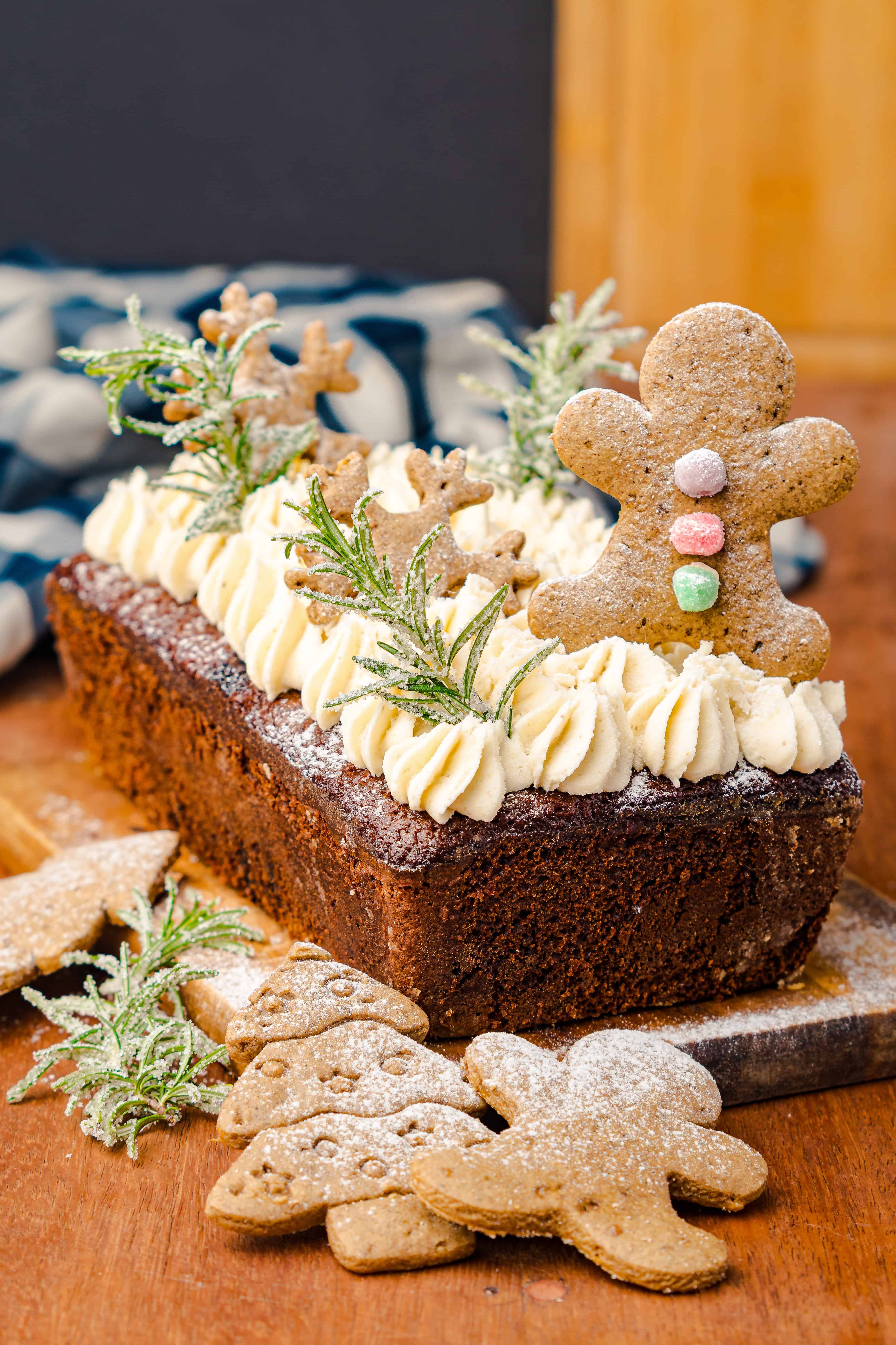 A Gingerbread Loaf topped with piped frosting, gingerbread cookies, and sugared herbs, served with extra cookies on the side.