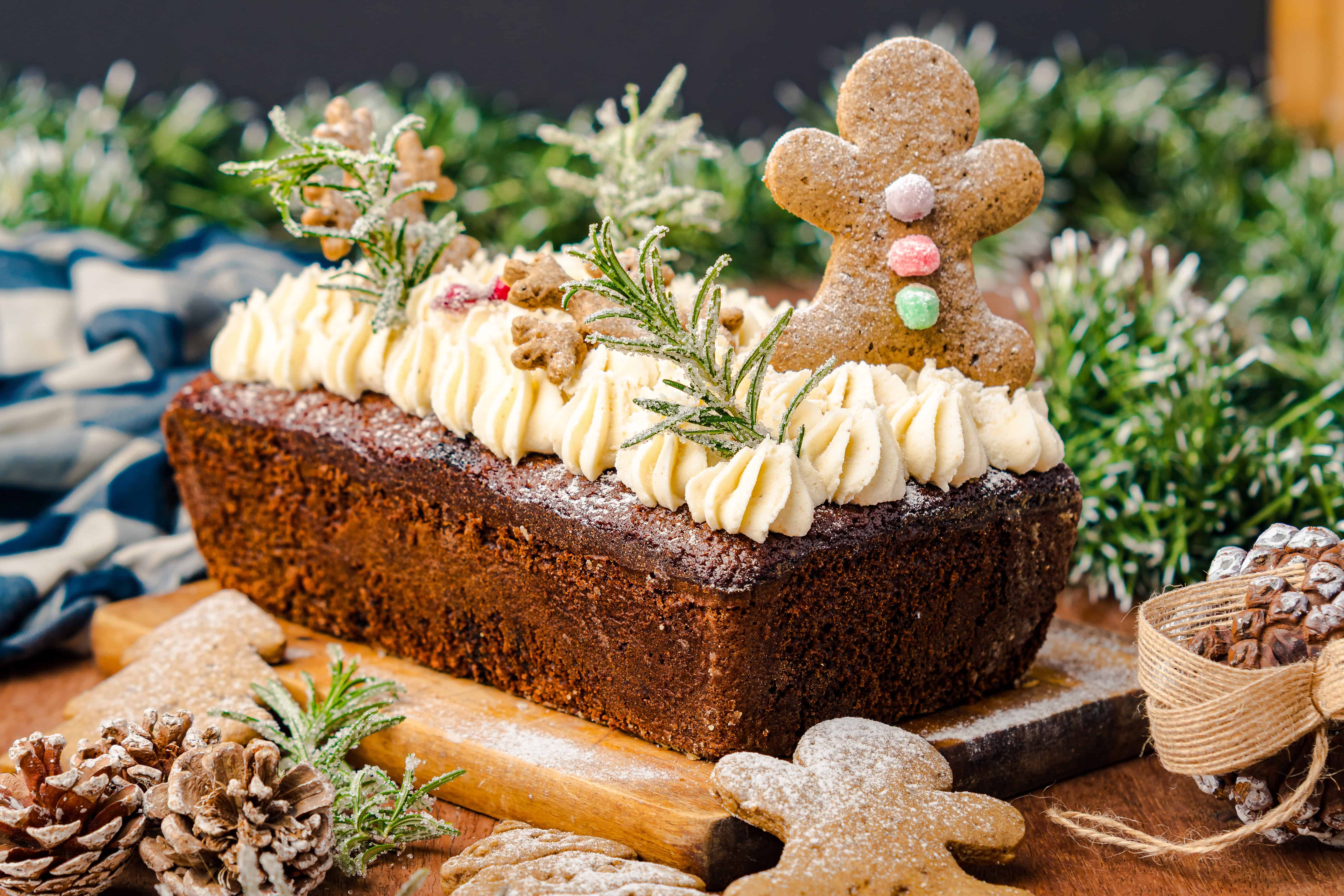 A festive Gingerbread Loaf topped with cream, rosemary, and a gingerbread man, surrounded by charming holiday decor.