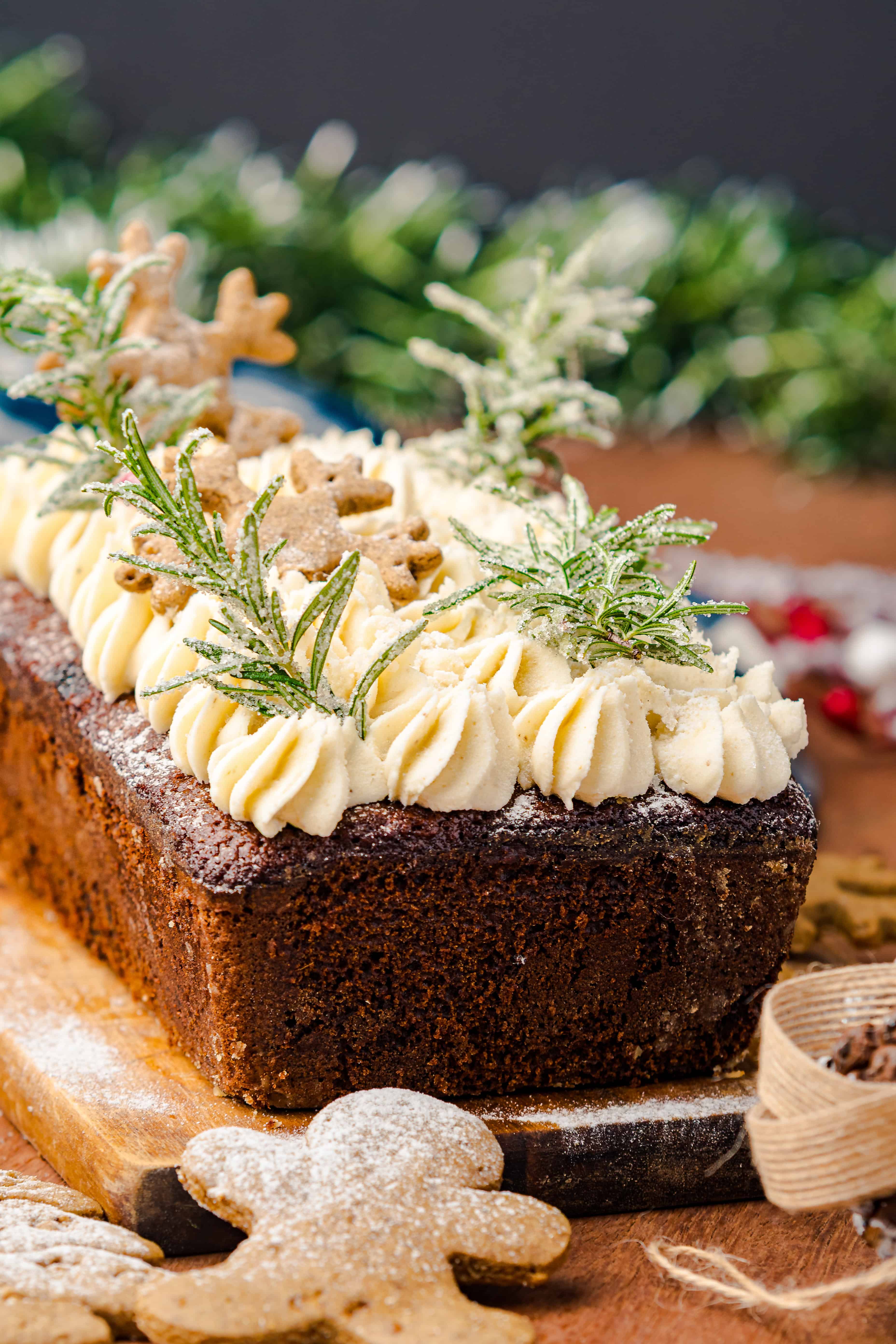 A festive Gingerbread Loaf cake decorated with piped cream, gingerbread cookies, and sugared rosemary on top.