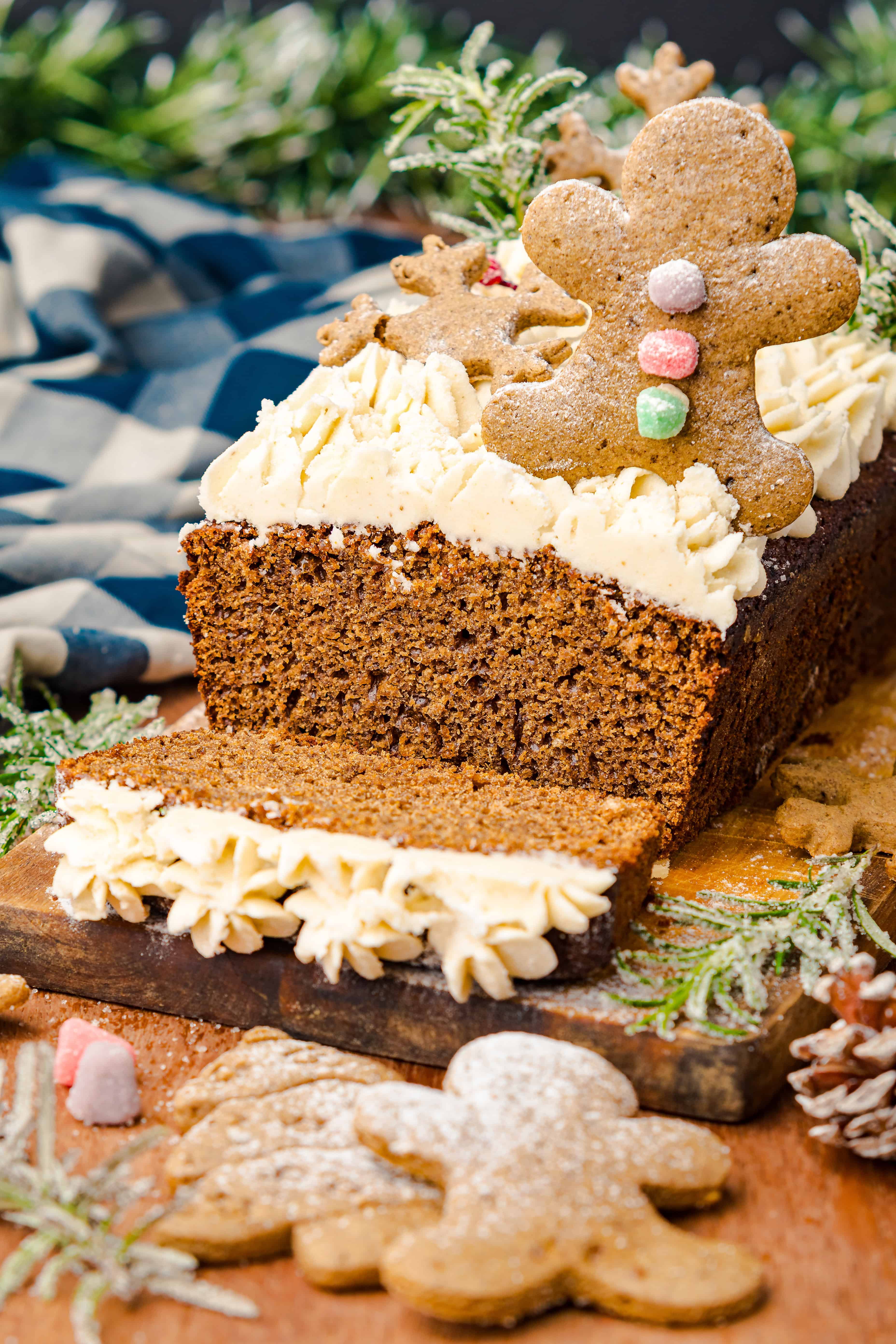 A sliced Gingerbread Loaf cake topped with frosting and gingerbread men cookies, surrounded by festive decor.