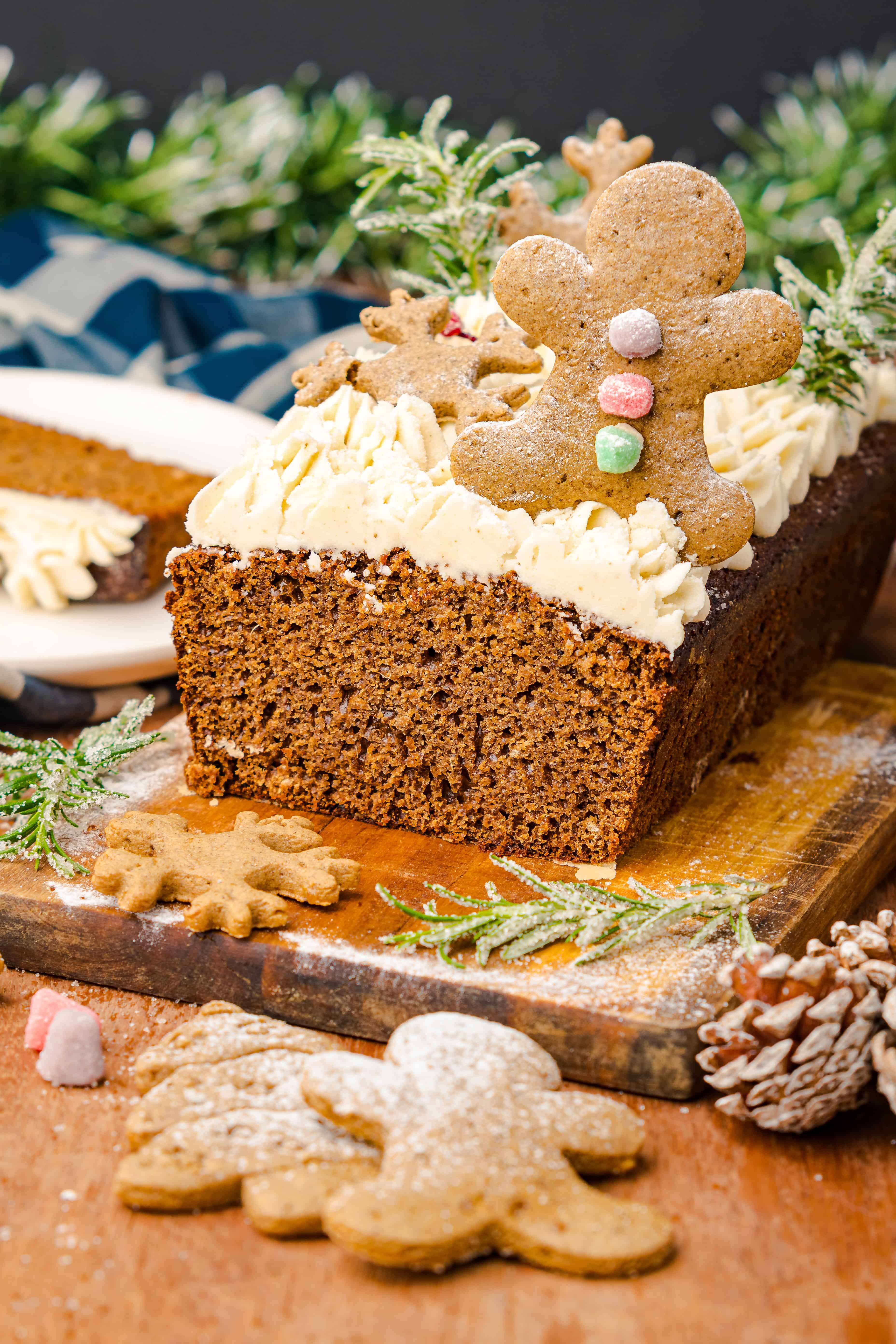 A festive Gingerbread Loaf cake topped with frosting and gingerbread cookies, surrounded by joyful holiday decorations.