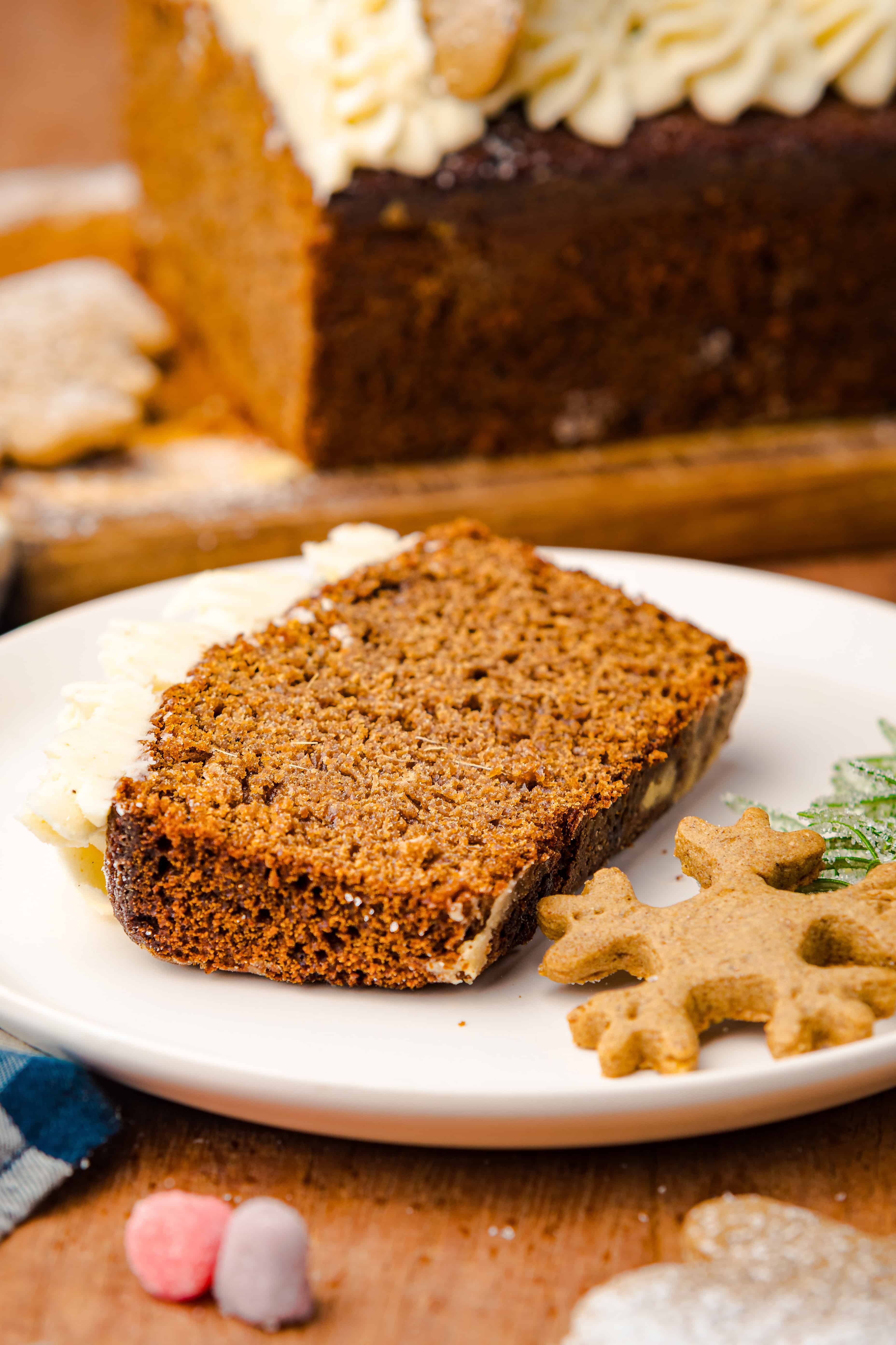 A slice of gingerbread loaf cake and a snowflake-shaped cookie rest on a white plate, capturing the cozy spirit of the season.