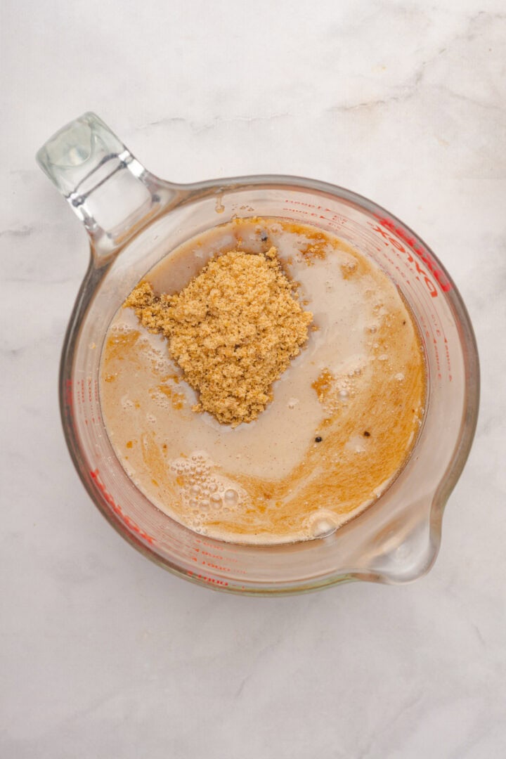 A glass measuring cup with brown sugar and liquid, perfect for preparing Gingerbread Loaf, sits on a white marble surface.