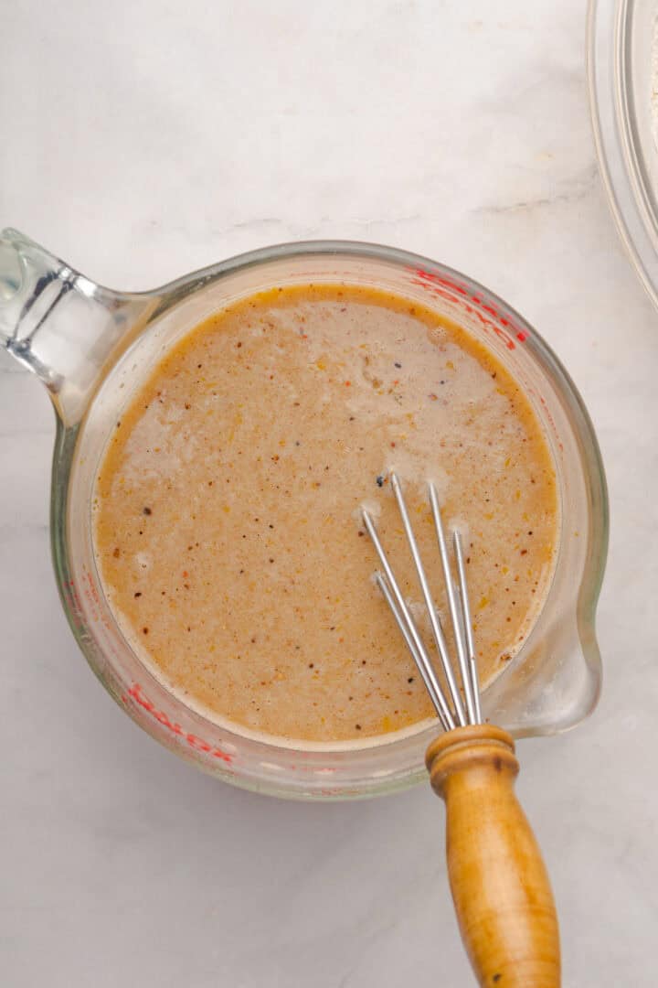 Glass measuring cup with seasoned liquid marinade and a small whisk with a wooden handle inside, ready for mixing flavors reminiscent of a Gingerbread Loaf.