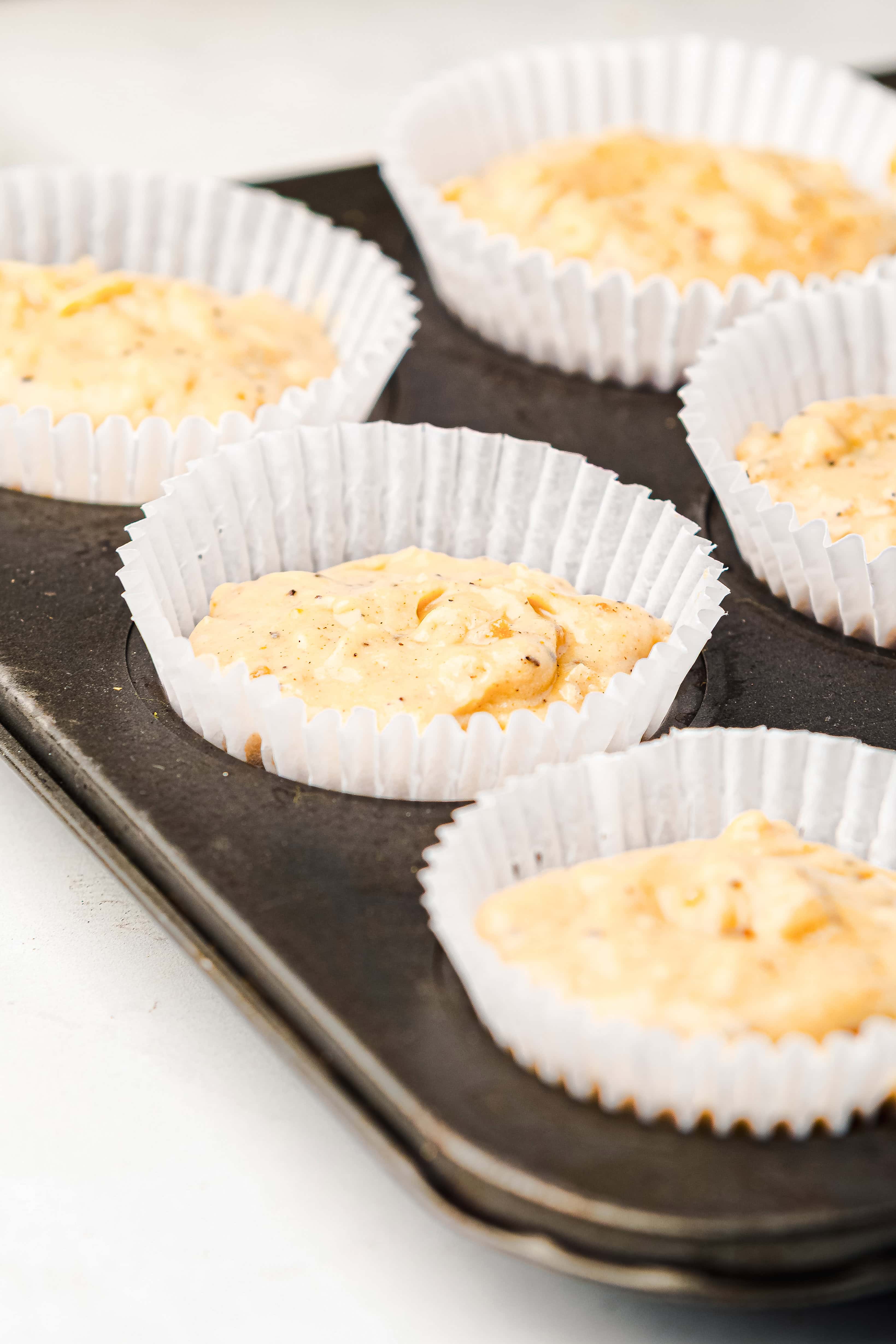 Unbaked gingerbread muffin batter in white paper liners sits inside a dark muffin tin, ready for baking.