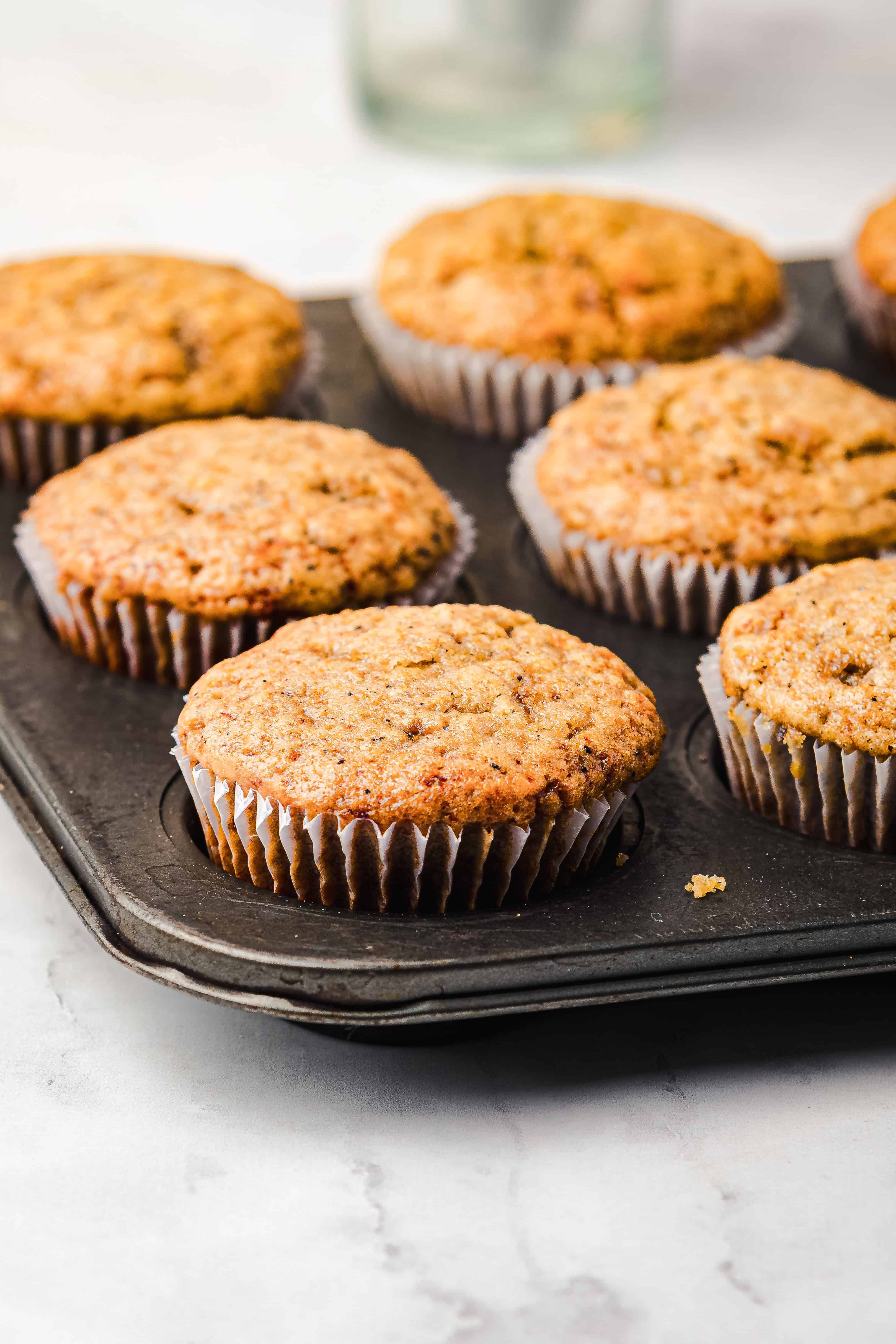 A muffin tin with six freshly baked gingerbread muffins in paper liners sits on a light countertop.