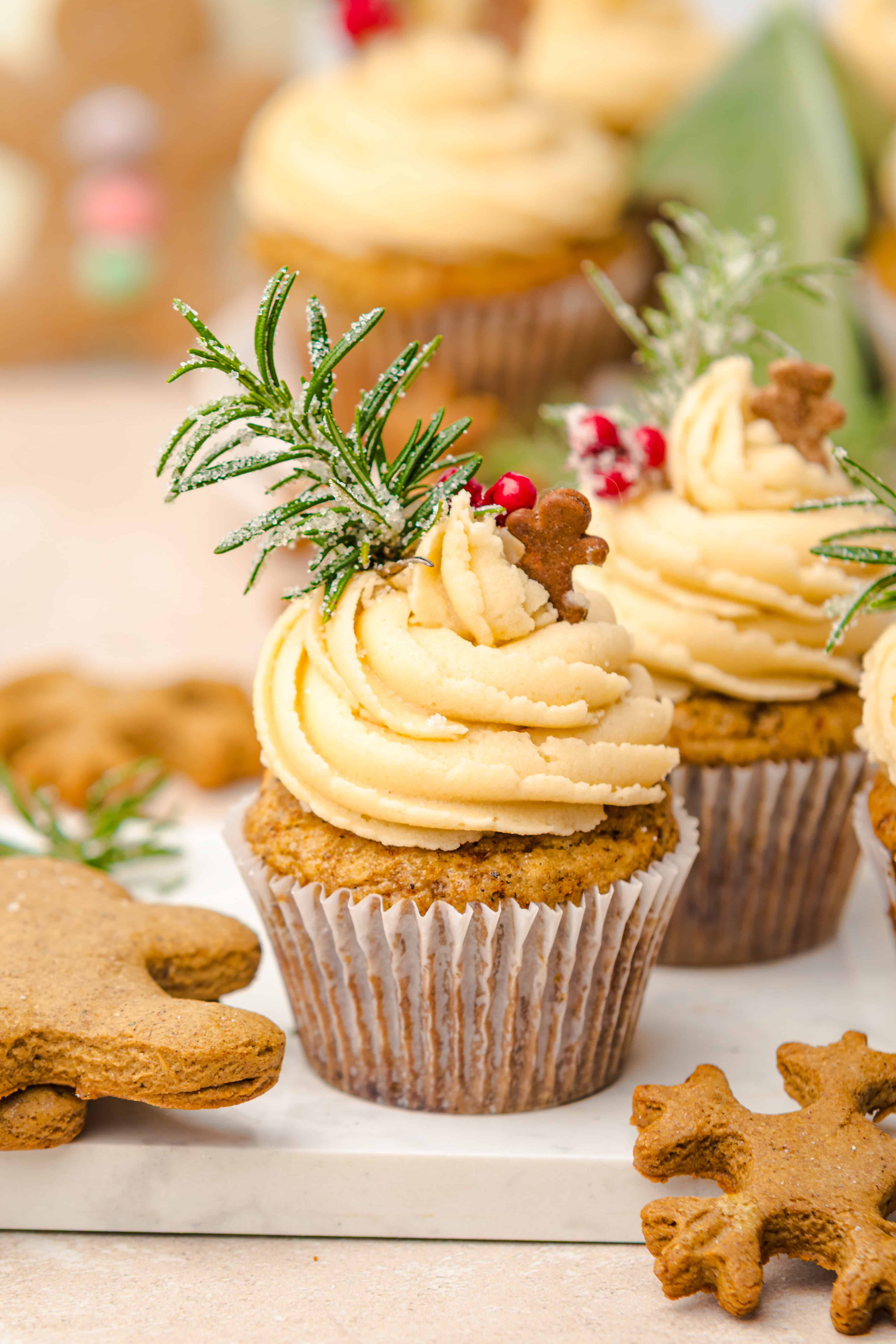 A festive cupcake with swirled frosting, rosemary, red berries, and a tiny gingerbread man on top—perfect for fans of gingerbread muffins.