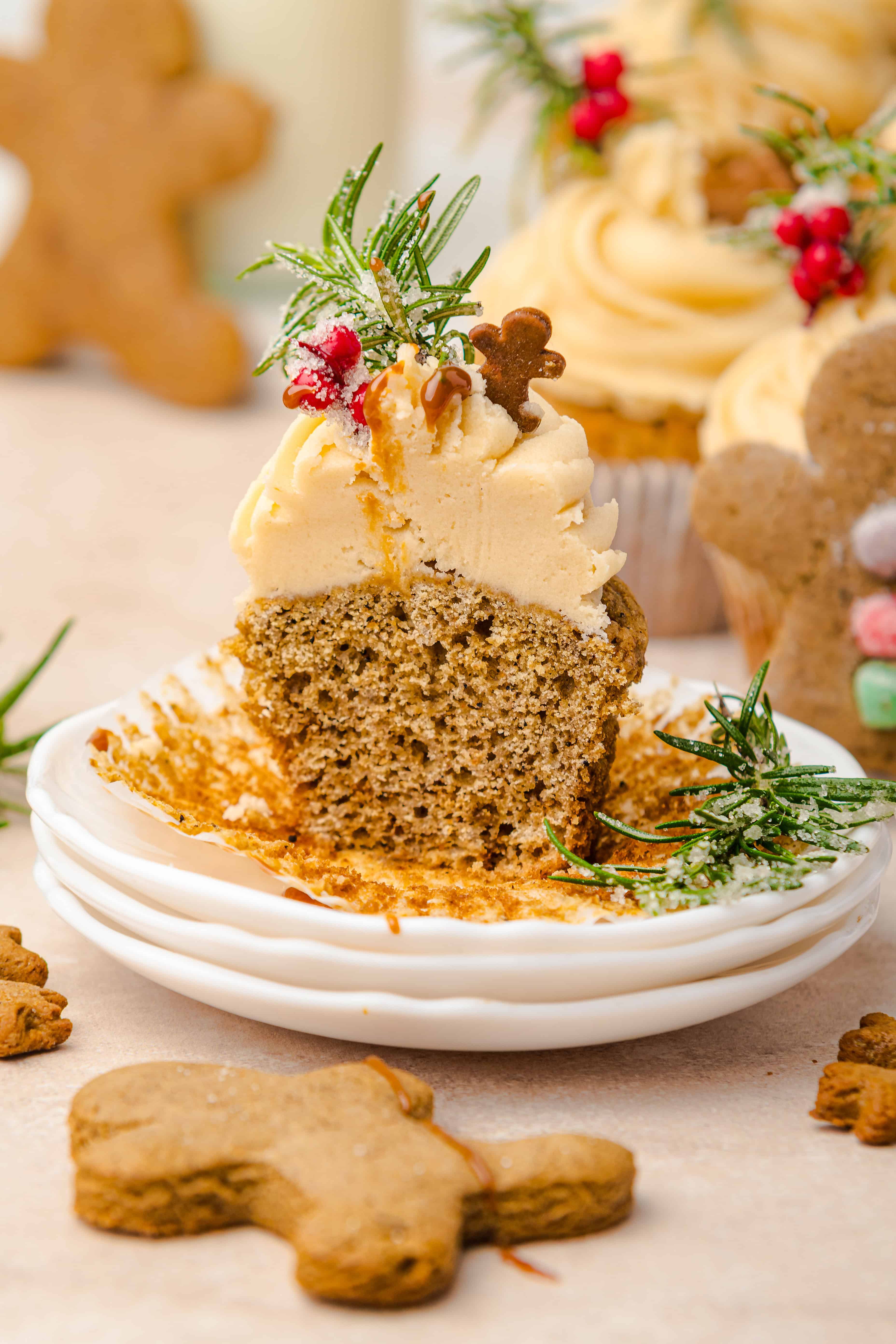 A spiced cupcake, reminiscent of gingerbread muffins, with beige frosting, cut in half and topped with herbs and a small gingerbread cookie.