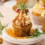 Cupcake with caramel drizzle, frosting, rosemary, and a small gingerbread cookie on a white plate—perfect for fans of gingerbread muffins.