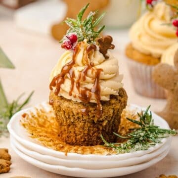 Cupcake with caramel drizzle, frosting, rosemary, and a small gingerbread cookie on a white plate-perfect for fans of gingerbread muffins.
